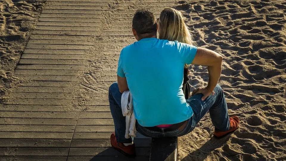 Dating Seiten in Österreich: ein Paar sitzt eng nebeneinander auf einem Holzsteg im Sand