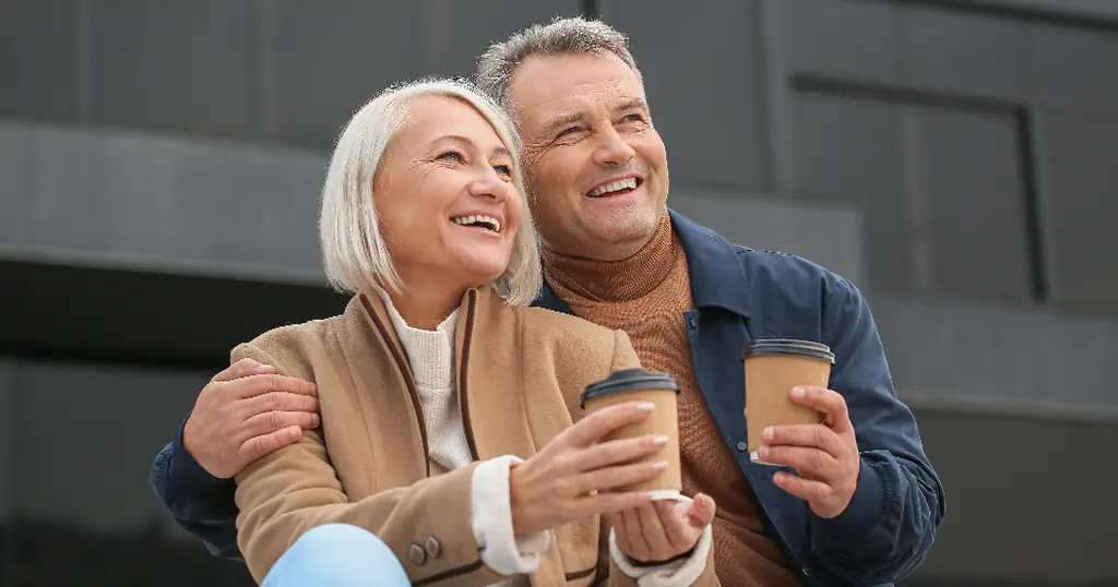 Partnersuche ab 50: ein lachendes älteres Paar mit Kaffeebechern in der Hand