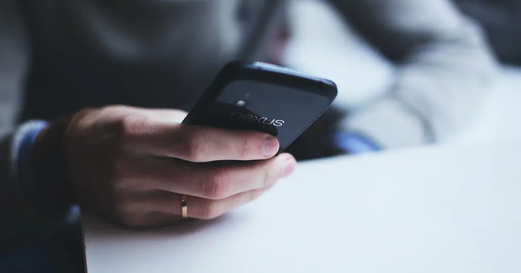 Dating-Profil Tipps: eine Person hält am Tisch ein Smartphone in der Hand