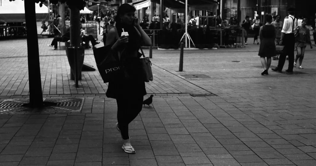 Love Scam erkennen: eine Frau geht mit dem Smartphone über eine belebte Straße