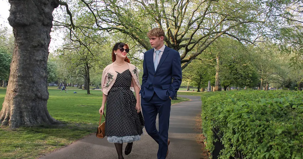 Dating Seiten: ein Paar spaziert Hand in Hand auf einem Parkweg zwischen Bäumen